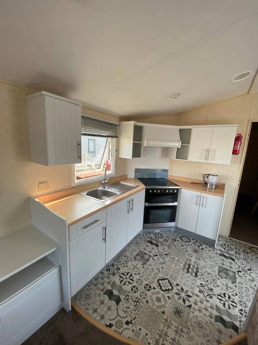 Finished caravan kitchen with white vertical-panel cabinets and a patterned floor